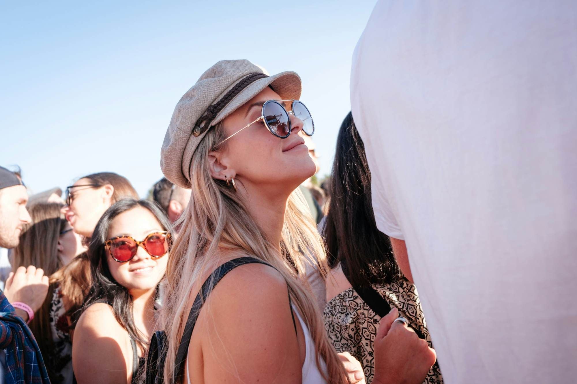 A woman wearing sunglasses and a hat smiling in a sunny outdoor crowd at VERVE Fayetteville.