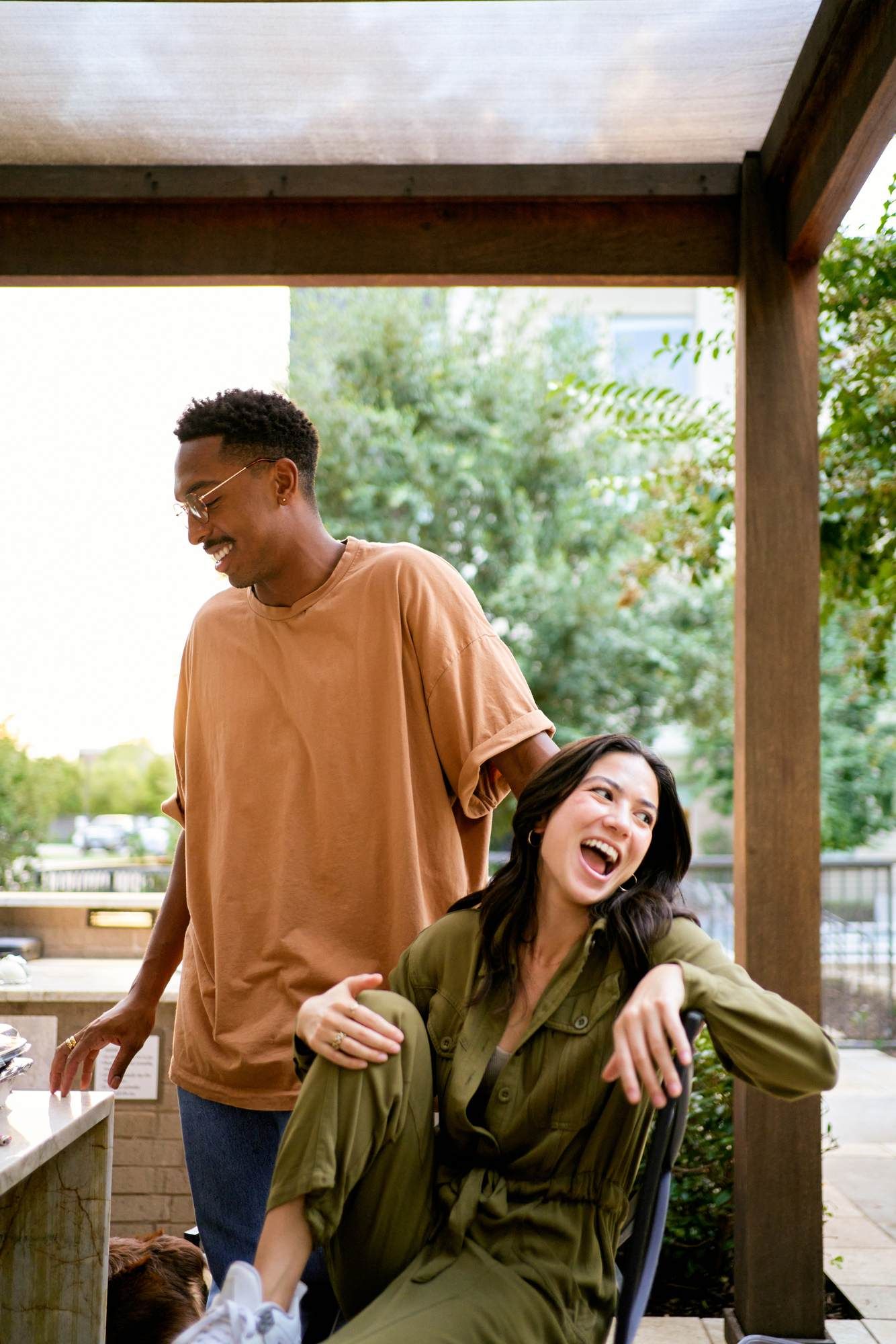 Two friends laughing together in bright sunlight, wearing sunglasses at VERVE Fayetteville.