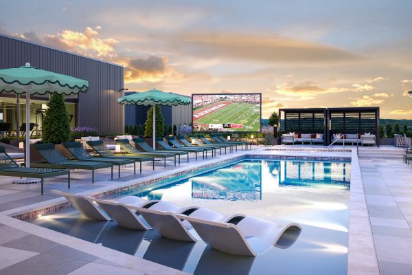 Rooftop pool with lounge chairs, green umbrellas, and a large outdoor screen showing a football game at sunset.