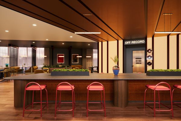 Modern lounge with a long wooden table, red stools, greenery, and a door labeled "Off Record" in the back.