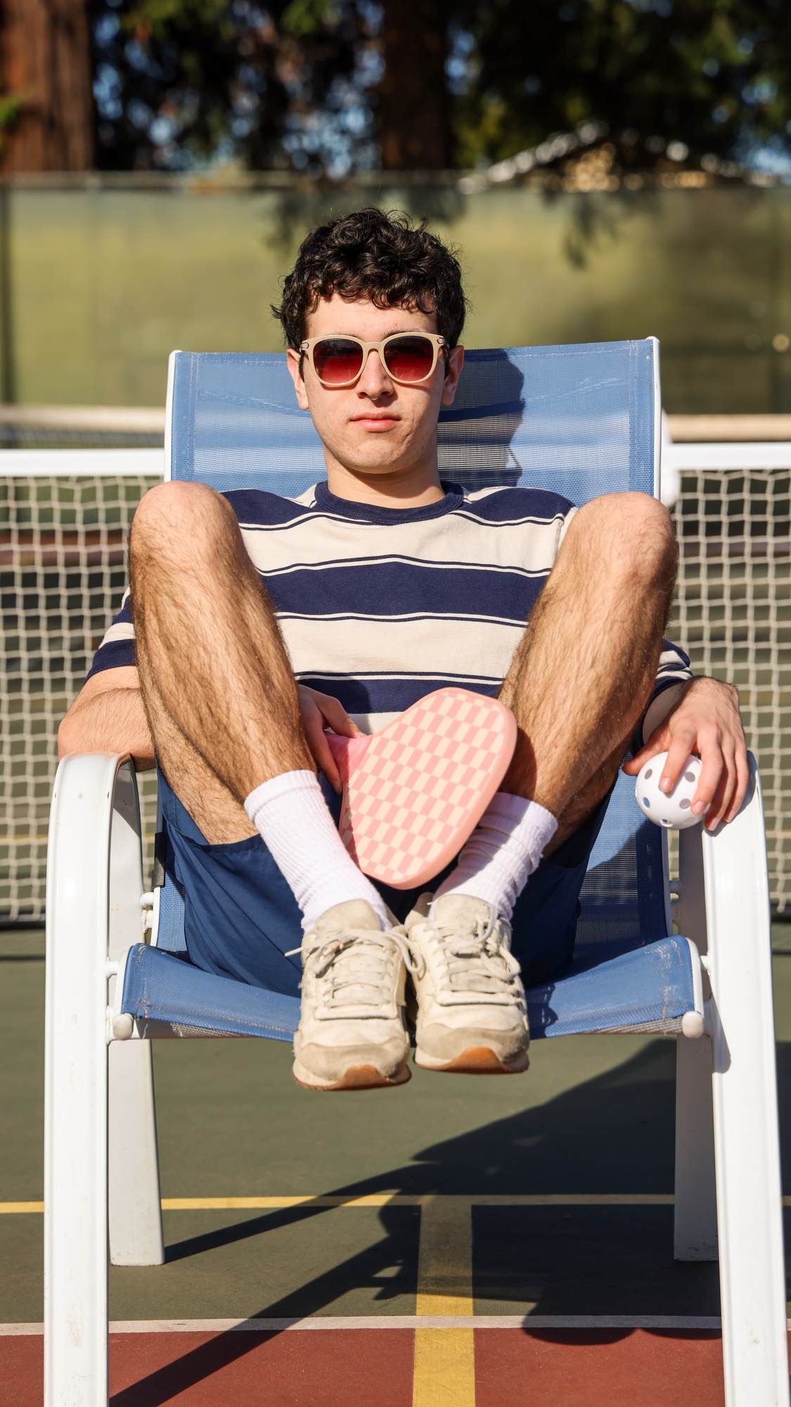A student relaxing on a lounge chair outdoors with sunglasses and a drink at VERVE Fayetteville.